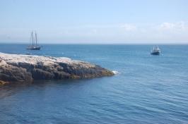 Rocky shoreline along the ocean with a boat and a sailboat in the background.
